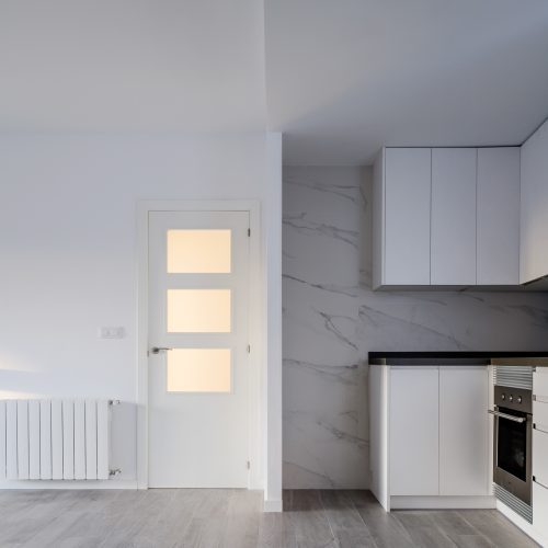 Vista interior de cocina blanca con suelo cerámico imitación madera proyectada por contratar arquitecto en Valencia