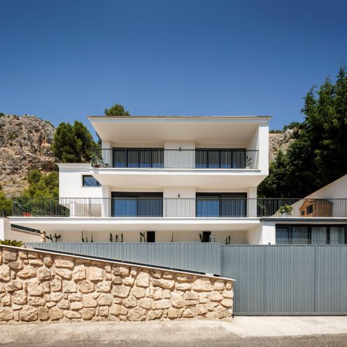 Arquitectura de calidad Valencia en vivienda unifamiliar con fachada geométrica, cerramiento metálico y ladera rocosa en Villa Muntanya