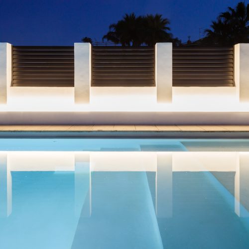 Iluminación lineal en cerramiento perimetral de piscina con reflejo arquitectónico diseñada por arquitectos Valencia