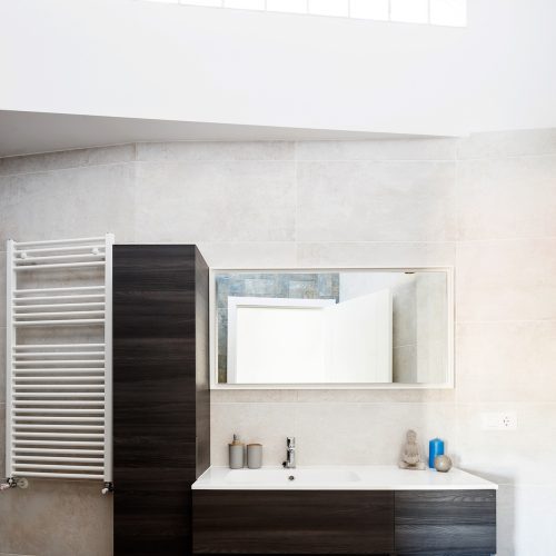 Baño con mobiliario suspendido en madera oscura, luz cenital y radiador toallero, reforma integral de piso en Valencia