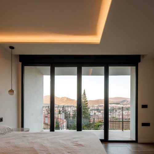 Arquitectura de calidad Valencia en dormitorio con apertura total, iluminación cenital indirecta y vistas al paisaje desde Villa Muntanya