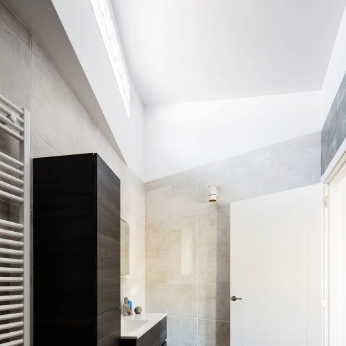 Baño con techo inclinado, entrada de luz por pavés y mobiliario suspendido, arquitectos Passivhaus en Valencia