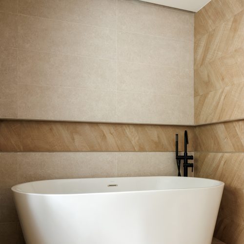 Bañera exenta blanca con grifería negra sobre pavimento cerámico efecto madera en baño proyectado con diseño de interiores sobrio