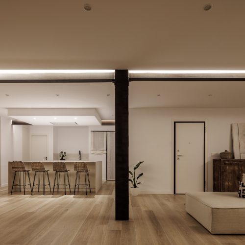 Vista nocturna de cocina abierta y entrada en vivienda diseñada por arquitecto de Valencia