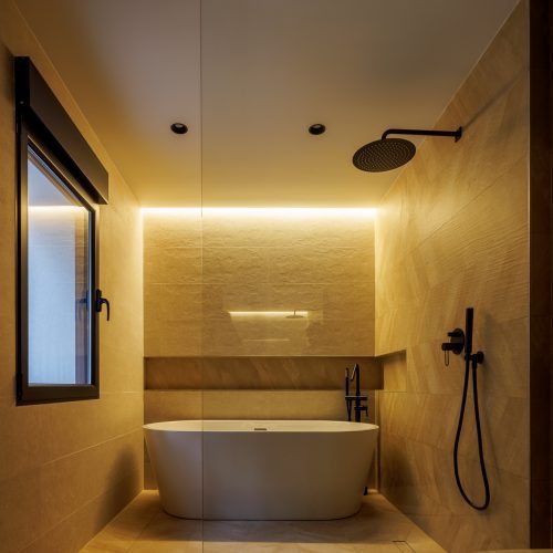 Zona de baño con bañera exenta, ducha y revestimientos cerámicos cálidos en reforma integral de vivienda unifamiliar