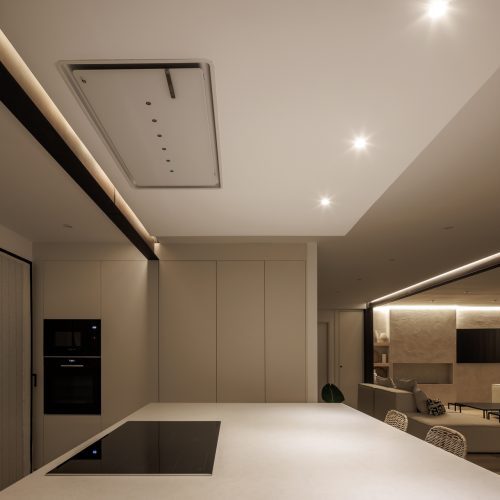 Perspectiva nocturna de cocina con isla y salón continuo proyectado por arquitectos Valencia
