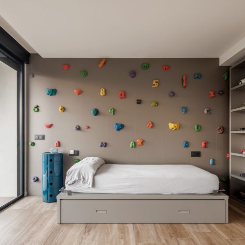 Dormitorio infantil con pared de escalada y mobiliario a medida en proyecto de arquitectura residencial en Alicante