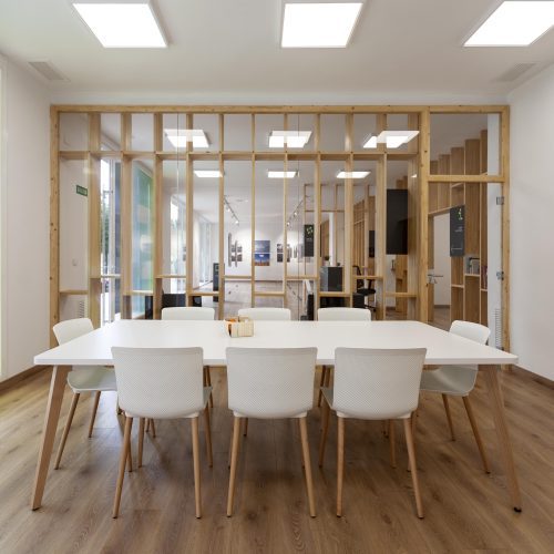 Sala polivalente con mobiliario blanco y cerramiento de madera diseñada por estudio de arquitectura en Valencia para uso institucional.