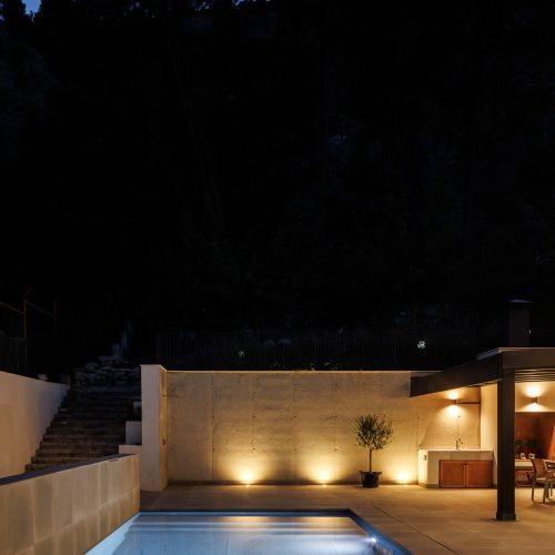 Piscina iluminada con zona de cocina exterior integrada en vivienda unifamiliar tras reforma arquitectónica en Valencia