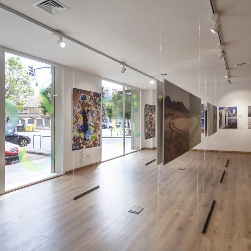 Vista de galería expositiva con fotografías suspendidas y fachada acristalada, diseñada por estudio de arquitectura Valencia.