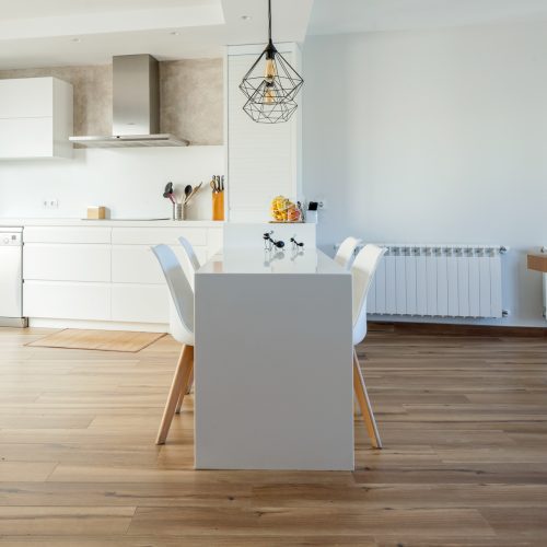 Cocina blanca integrada con comedor y pavimento de madera continua, estudio de arquitectura Valencia