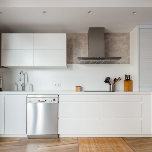 Cocina blanca con mobiliario sin tiradores, campana vista y muro de piedra, mejores arquitectos en Valencia