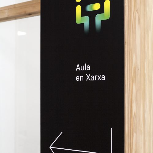 Detalle de señalética interior en madera natural, resuelta por arquitecto de calidad Valencia con lenguaje gráfico accesible.