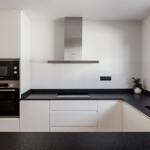 Cocina en U con mobiliario blanco y encimera negra proyectada por contratar arquitecto en Valencia