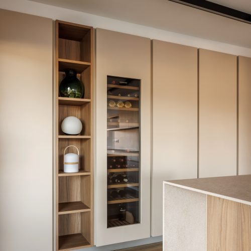 Arquitectura aplicada al diseño interior con frente de cocina, bodega integrada y estantería en madera natural en vivienda Villa Muntanya