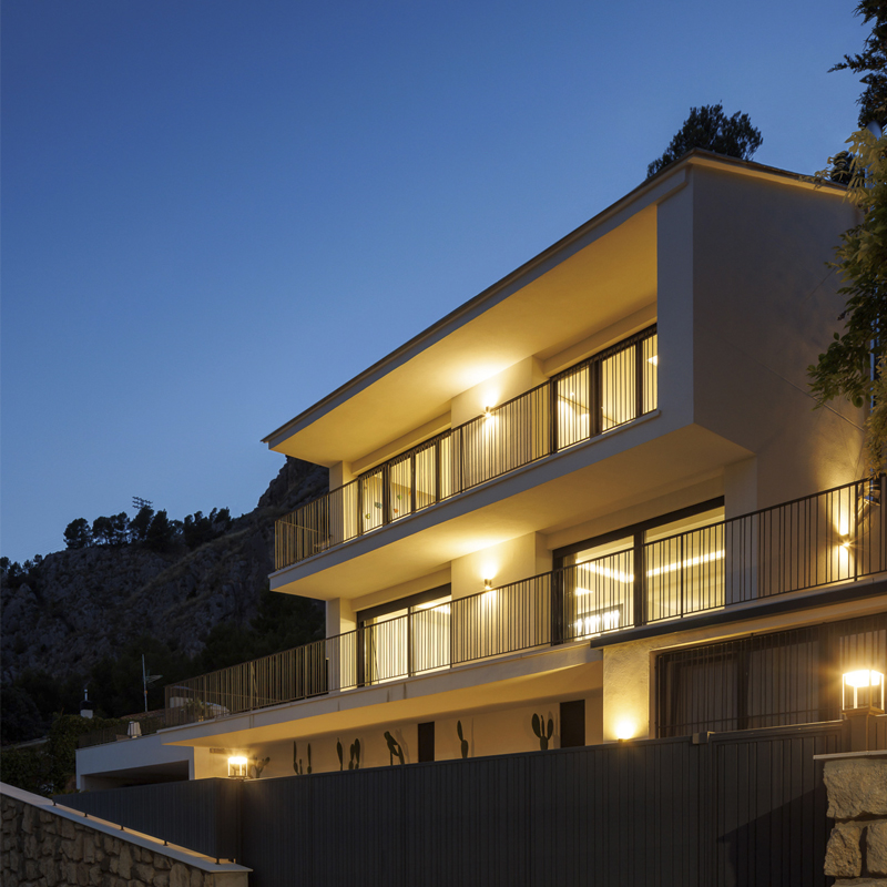 Fachada iluminada de vivienda unifamiliar tras rehabilitación de viviendas en altura, con barandillas metálicas y triple nivel en Villa Muntanya