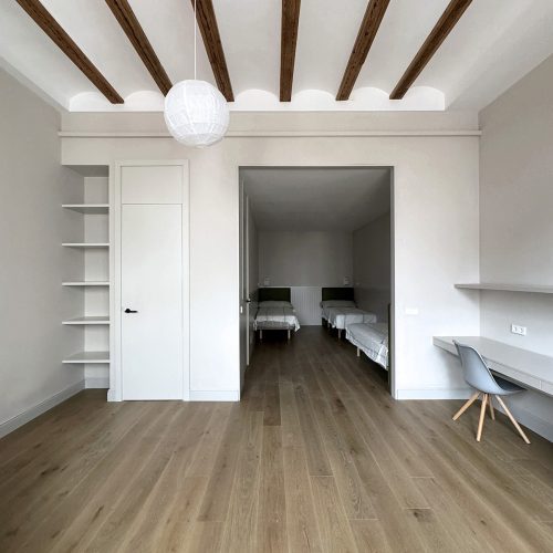 Dormitorio infantil con pavimento de madera natural y techos con vigas vistas en vivienda reformada en el Eixample de Valencia