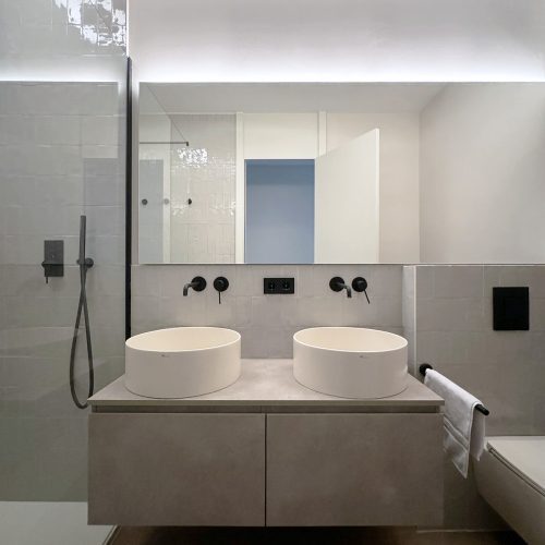 Lavabo doble suspendido con grifería negra empotrada en baño reformado durante reforma integral de vivienda en Gran Vía, Valencia