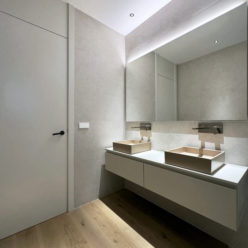 Baño secundario incluido en proyecto de arquitectura de interiores con lavabos sobreencimera y mobiliario suspendido en Gran Vía, Valencia