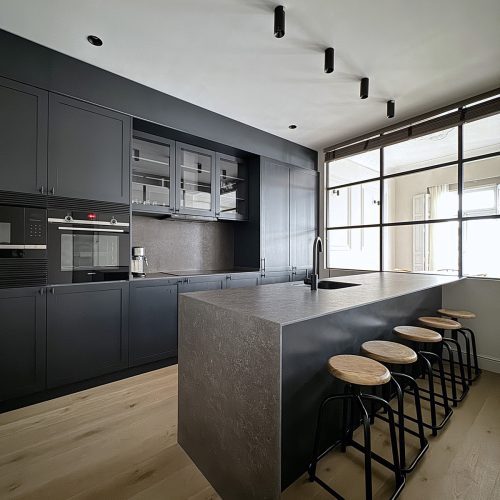 Cocina con isla de piedra y mobiliario negro mate dentro de proyecto de diseño de interiores en vivienda reformada en Gran Vía, Valencia