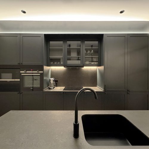 Cocina negra con encimera de piedra, grifería empotrada e iluminación integrada en proyecto de interiorismo residencial en Valencia