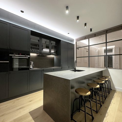 Cocina con isla central, mobiliario negro mate e iluminación técnica en proyecto de diseño arquitectónico en piso reformado en Valencia