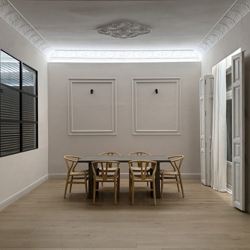 Comedor con molduras originales, luz perimetral y mampara metálica, integrado en proyecto de diseño de viviendas en piso reformado en Valencia