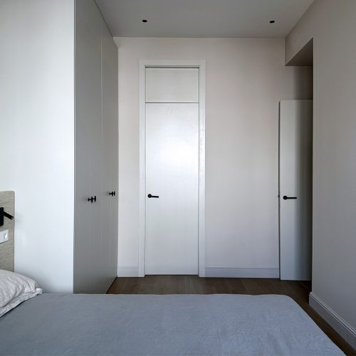 Dormitorio principal con armarios a medida, puertas integradas y cabecero textil en proyecto de interiorismo residencial en vivienda de Valencia