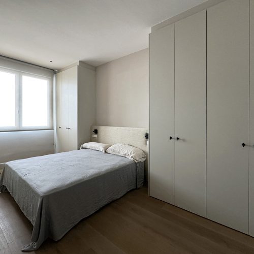 Dormitorio principal con armarios empotrados, cabecero textil y luz natural en proyecto de arquitectura residencial en vivienda reformada en Valencia