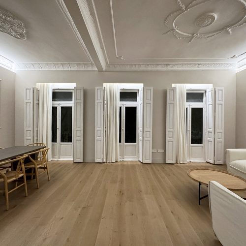 Salón-comedor con carpinterías originales, molduras restauradas y rosetón ornamental, ejemplo de arquitectura clásica en vivienda de Valencia