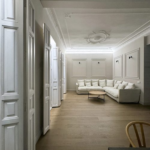 Vista longitudinal del salón con molduras restauradas, carpinterías clásicas y mobiliario neutro en proyecto de Alfaro Arquitectos – Estudio de arquitectura en Valencia