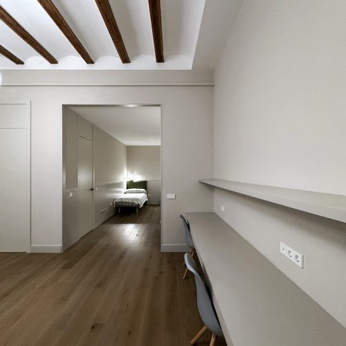 Zona de estudio con vigas vistas, escritorio doble y pavimento continuo en proyecto de interiorismo residencial en vivienda reformada en Valencia