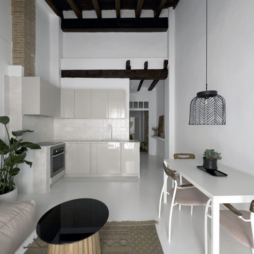 Espacio abierto con cocina integrada, comedor y vigas originales restauradas en intervención de diseño de interiores en vivienda rehabilitada