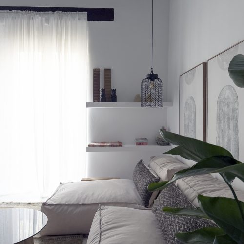 Zona de estar con sofá modular, vigas de madera restauradas y decoración sobria en intervención de interiorismo residencial