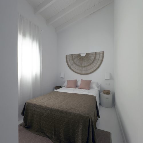 Dormitorio principal con techo a dos aguas de madera restaurado y textiles neutros en proyecto de rehabilitación de viviendas por arquitecto Valencia