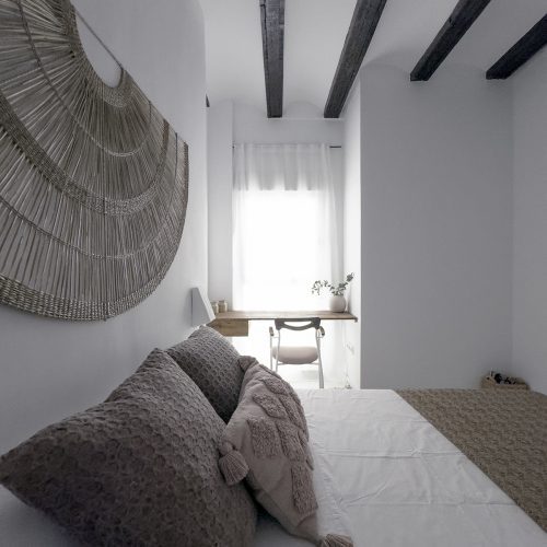 Dormitorio con vigas restauradas, textiles neutros y escritorio empotrado en proyecto de arquitectura de interiores por arquitectos Valencia