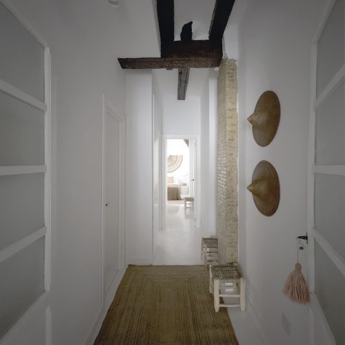 Pasillo rehabilitado con vigas estructurales originales y muro de ladrillo visto en proyecto de arquitecto residencial en Ciutat Vella