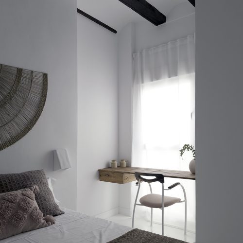 Dormitorio con vigas de madera originales, escritorio a medida y textiles neutros en proyecto de arquitectura de interiores en Valencia