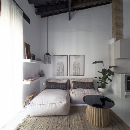Salón con sofás bajos, techo de vigas restauradas y elementos originales expuestos en intervención de interiorismo residencial en Valencia