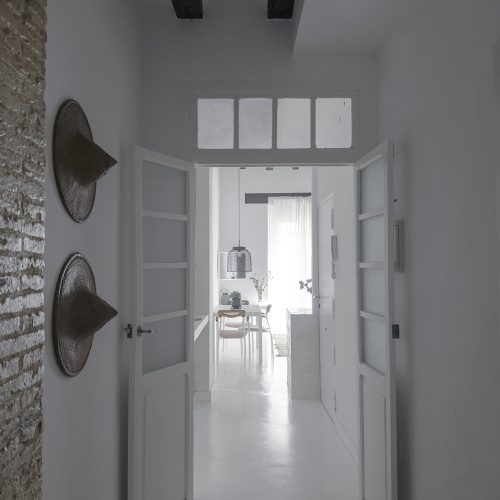 Pasillo con pavimento continuo, carpinterías restauradas y elementos originales expuestos en arquitectura residencial en Valencia