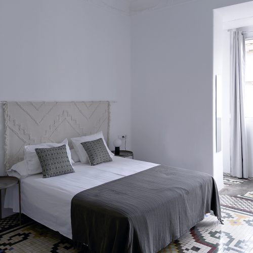 Dormitorio restaurado con pavimento de mosaico, molduras originales y mobiliario sobrio en proyecto de interiorismo residencial