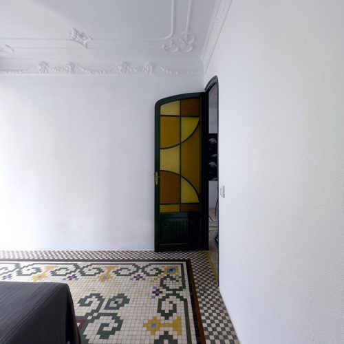 Puerta con vidriera de tonos cálidos y suelo hidráulico con motivo vegetal restaurado en reforma de vivienda en El Mercat, Valencia