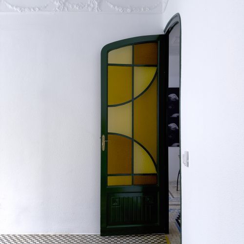 Puerta vidriada restaurada con carpintería verde, mosaico hidráulico floral y molduras de escayola en intervención de arquitectura de calidad en Valencia