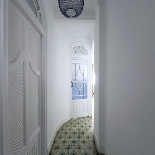 Pasillo curvo con pavimento hidráulico original y puertas restauradas con vidrio esmerilado en proyecto de rehabilitación energética en Ciutat Vella