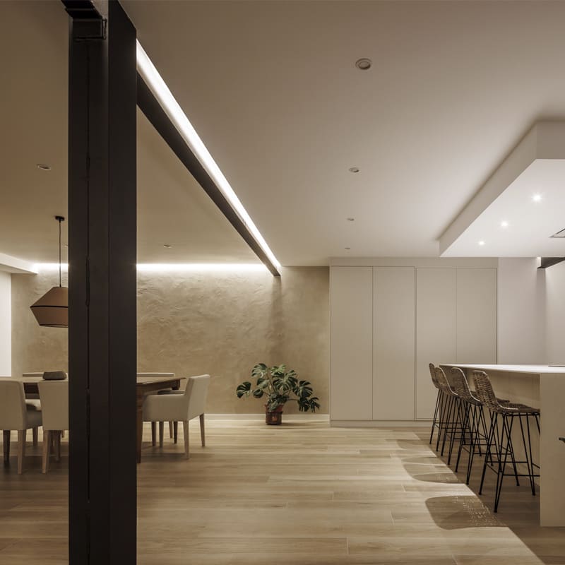 Salón comedor y cocina en planta abierta con pilar metálico visto y pared de mortero de arcilla, reforma integral de vivienda en Alcoy, Alicante